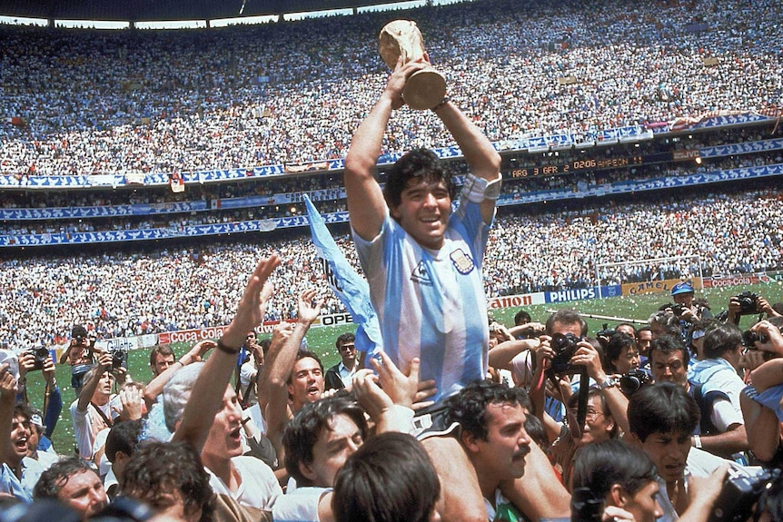 Diego Maradona lifts the FIFA World Cup trophy as his Argentina teammates lift him on their shoulders.