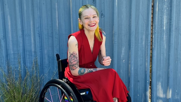 A blonde woman in a bright red dress, in a wheelchair, smiles widely