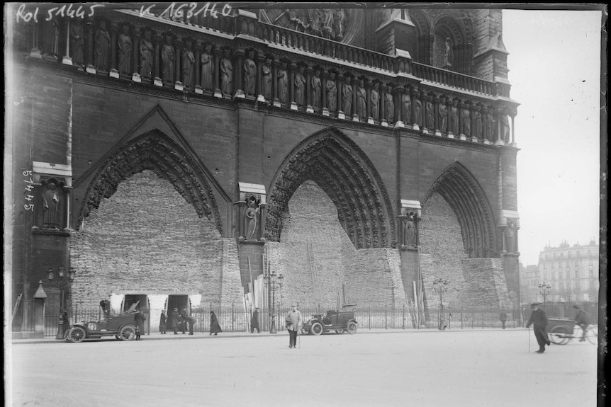 An old photo shows people and cars outside Notre Dame cathedral.