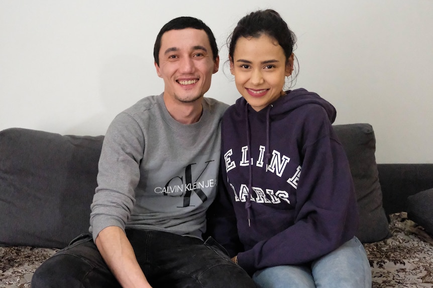 Sadam Abdusalam and his wife Nadila smiling and sitting on couch.