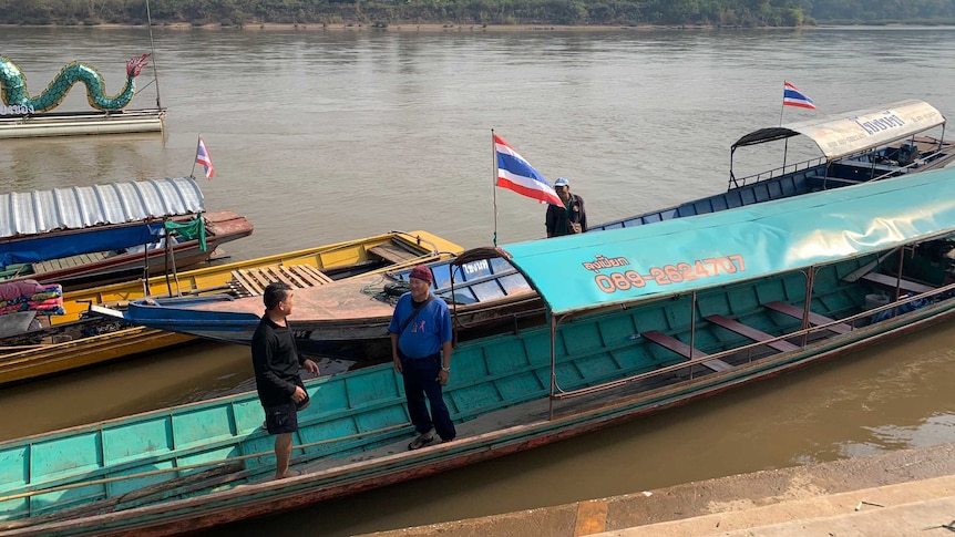 Two fishermen stand and talk in their boats on the Mekong River.