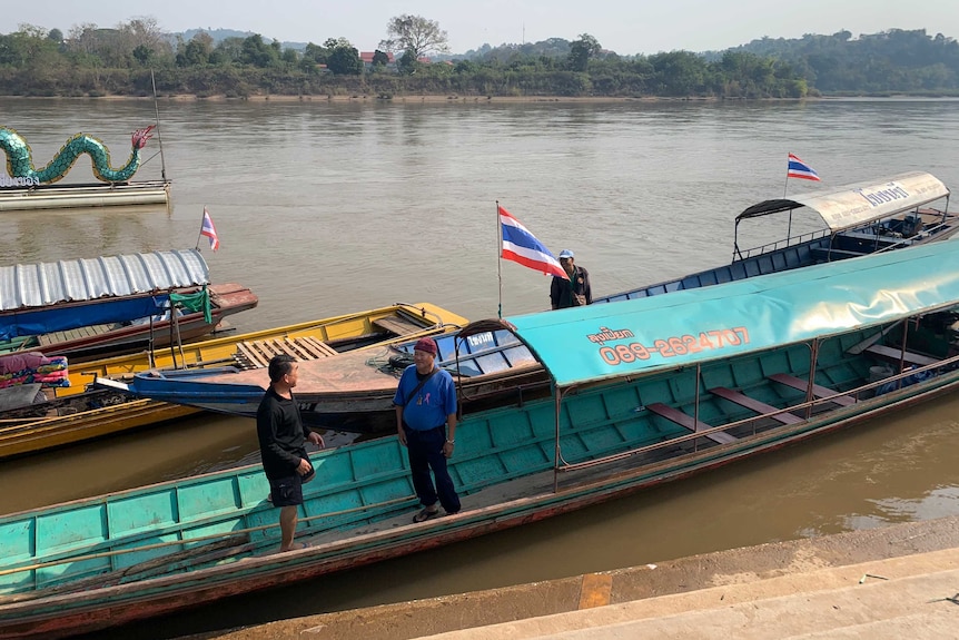 Two fishermen stand and talk in their boats on the Mekong River.
