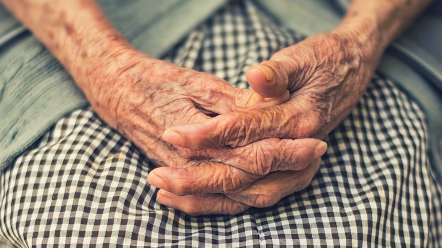 An elderly woman sits with her hands in her lap.