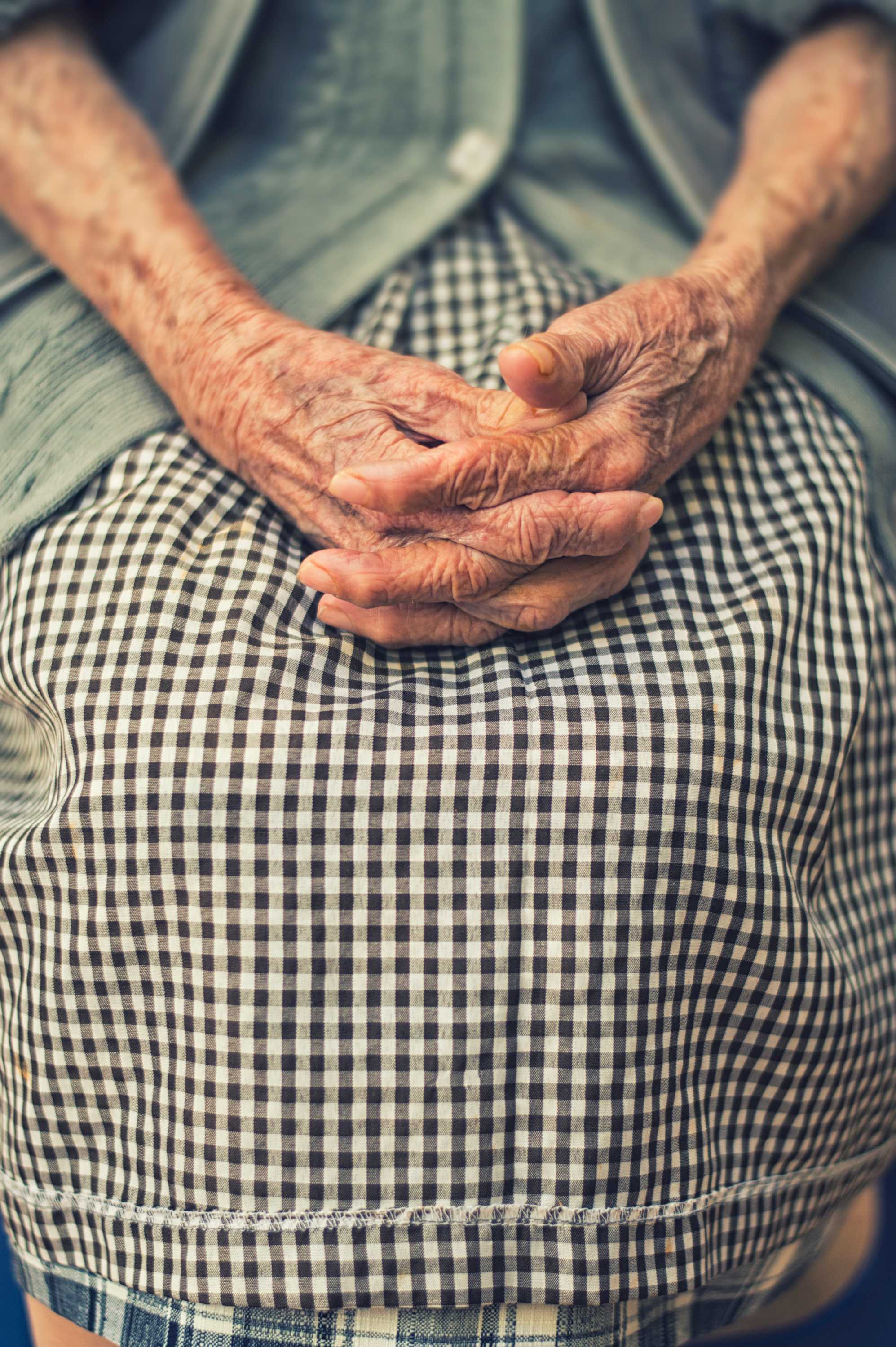 一位老妇人双手放在膝上坐着。