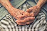 An elderly woman sits with her hands in her lap. Elderley generic