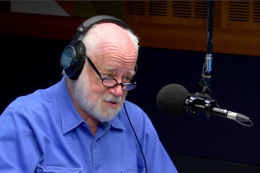 Adams with headphones on sitting in studio talking into microphone.