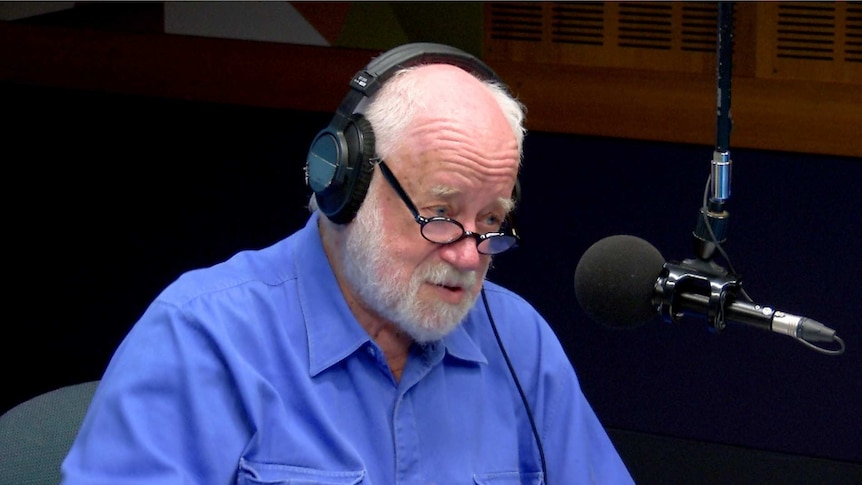 Adams with headphones on sitting in studio talking into microphone.