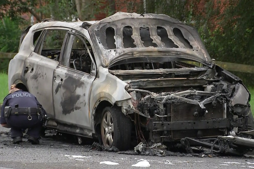 a police person standing next to a torched car