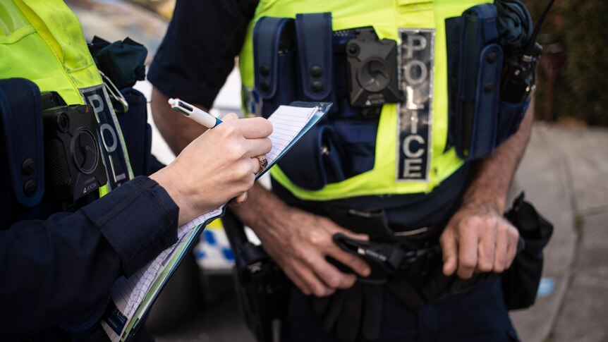 Two police officers stand together - one of them writes on a notepad.