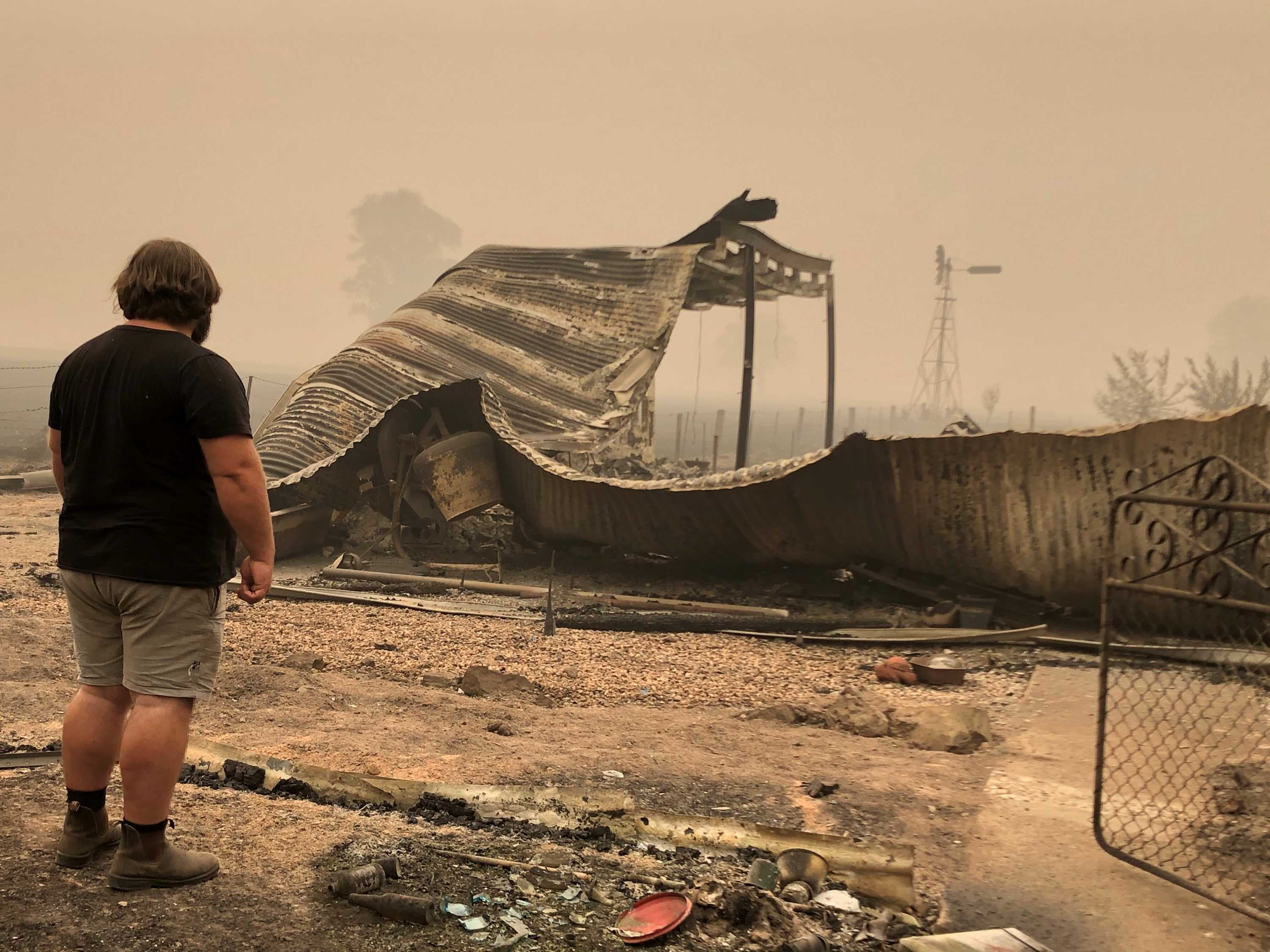 A man shown from behind looking at the remains of his fire-damaged property.