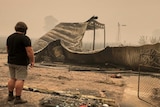 A man shown from behind looking at the remains of his fire-damaged property.