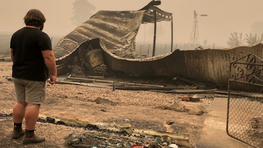 A man shown from behind looking at the remains of his fire-damaged property.