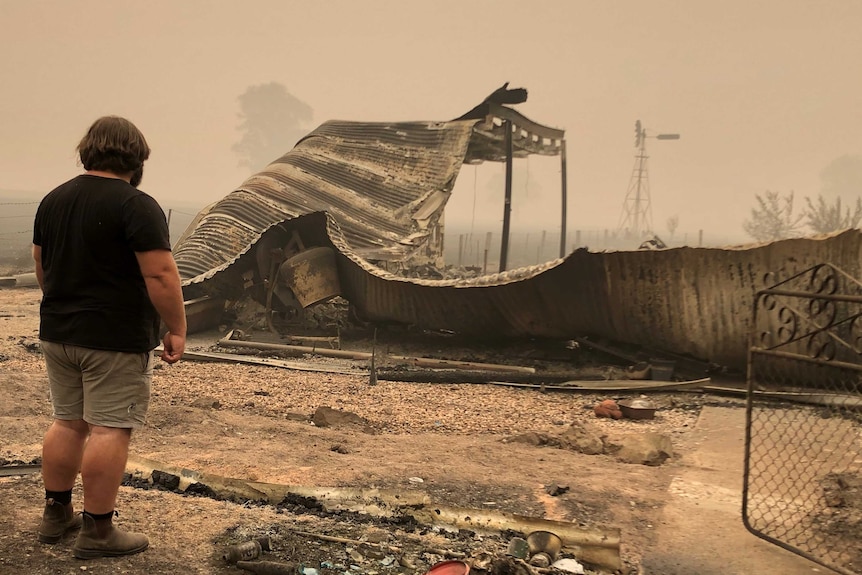 A man shown from behind looking at the remains of his fire-damaged property.