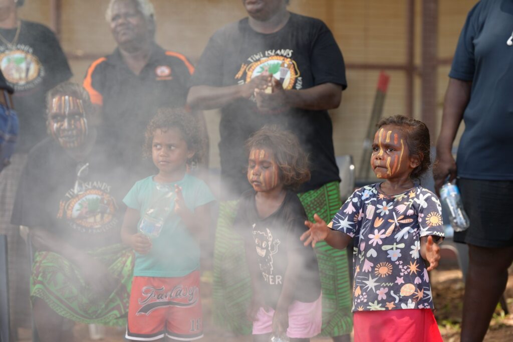 Young Indigenous girl puts hands out next to waft of smoke during traditional ceremony