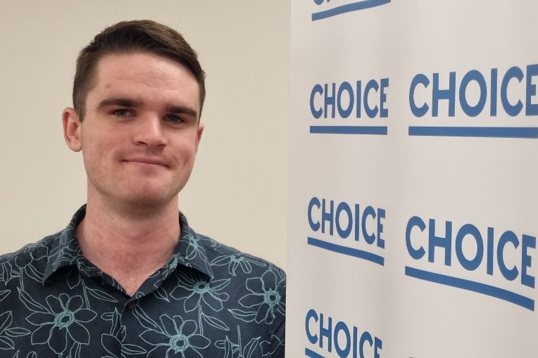 Liam Kennedy viste una camisa azul con flores de un azul más claro y está de pie junto a una pancarta con el logo de Choice.