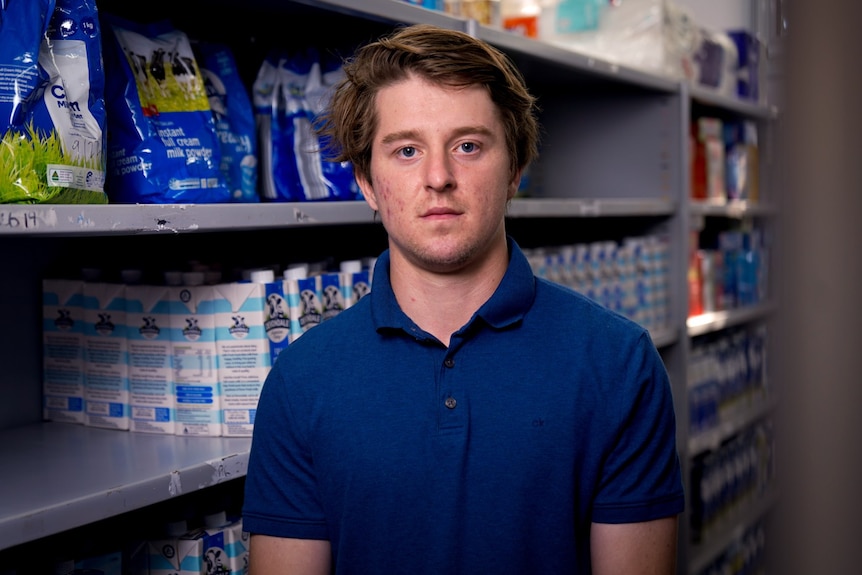 A man in a blue shit stands in an aisle of food.