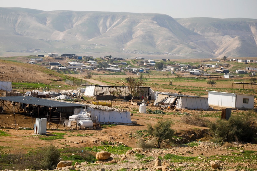 A seris of makeshift camps sprawled across brown green land against a mountainous landscape