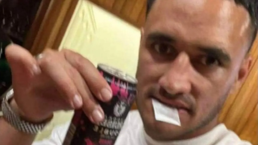 A slightly blurry image of a man holding a bag of white powder between his lips while holding up a drink can.