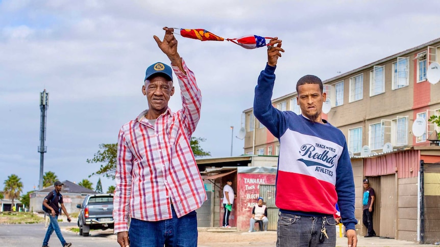 Two men standing in the street holding facemasks in air