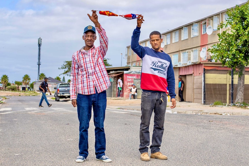 Two men standing in the street holding facemasks in air