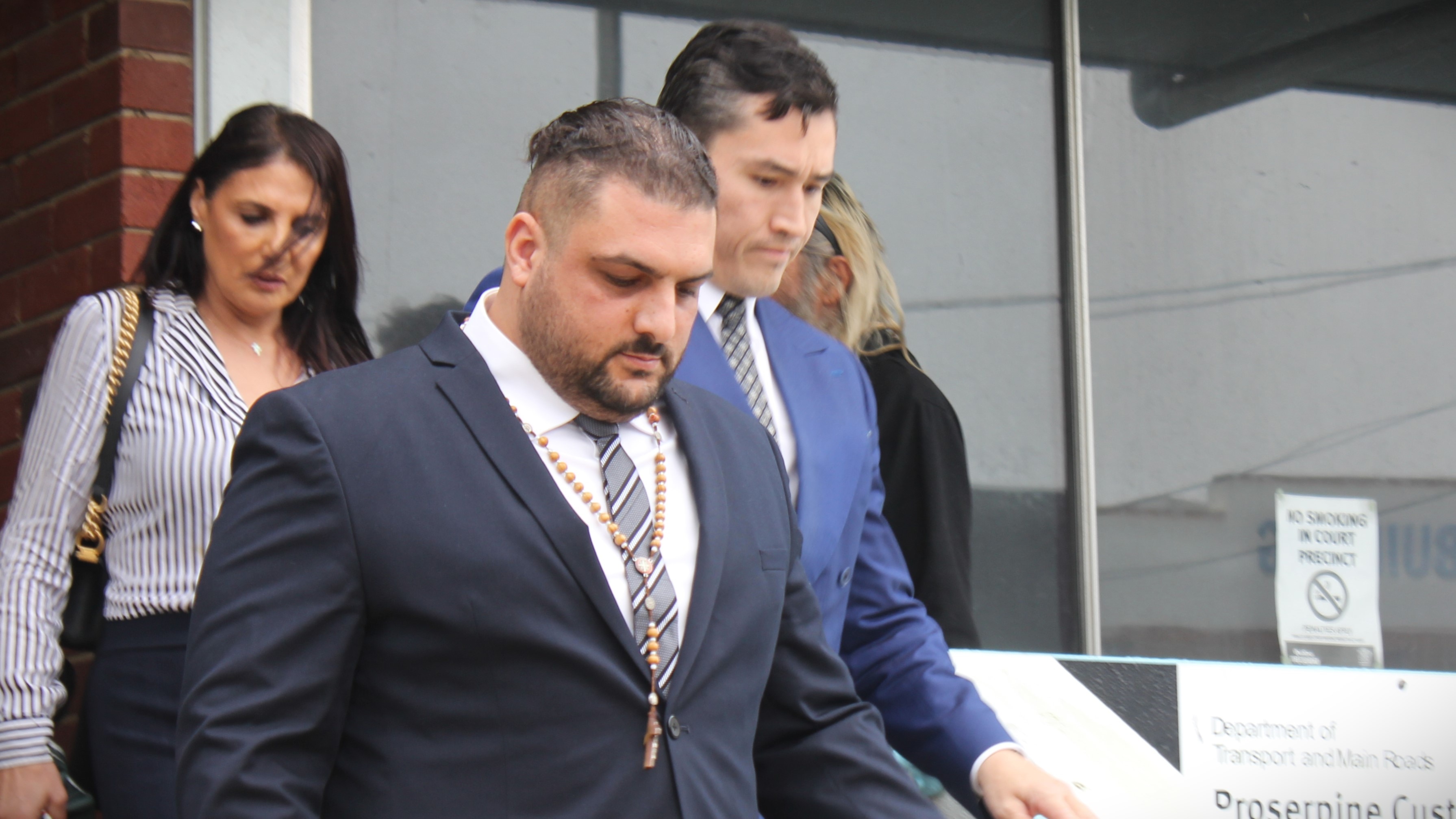 Man in suit with rosary beads around neck walking out of courthouse 