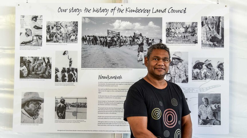 Anthony Watson stands in front of a board with pictures and words detailing the history of the Kimberley Land Council.