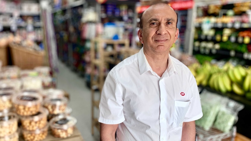 IGA owner Iftkhar Khan stands in his store in front of groceries on shelves.