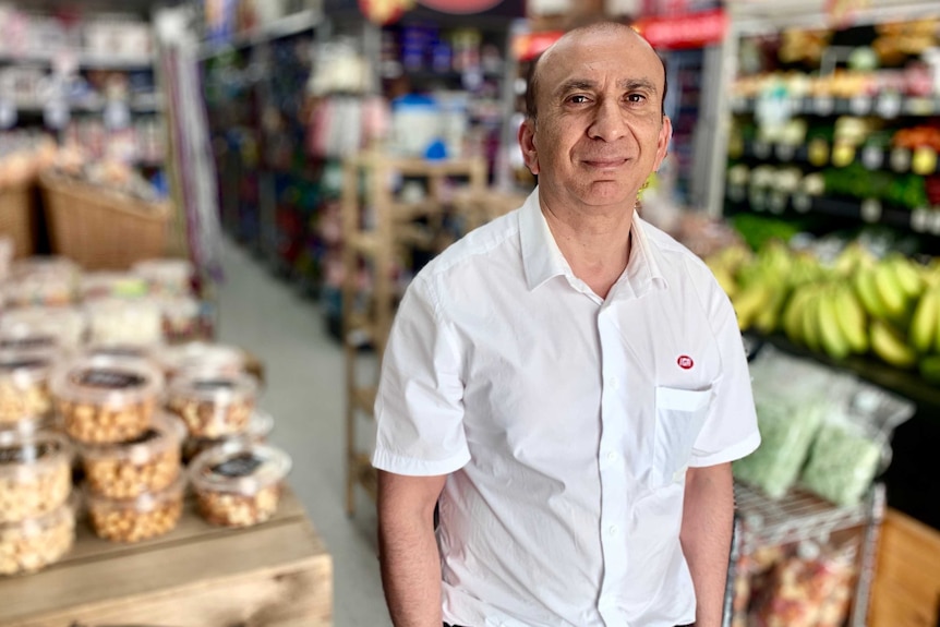 IGA owner Iftkhar Khan stands in his store in front of groceries on shelves.