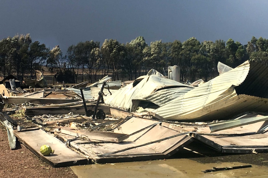 Corrugated iron sheets and debris lie scattered on the ground.