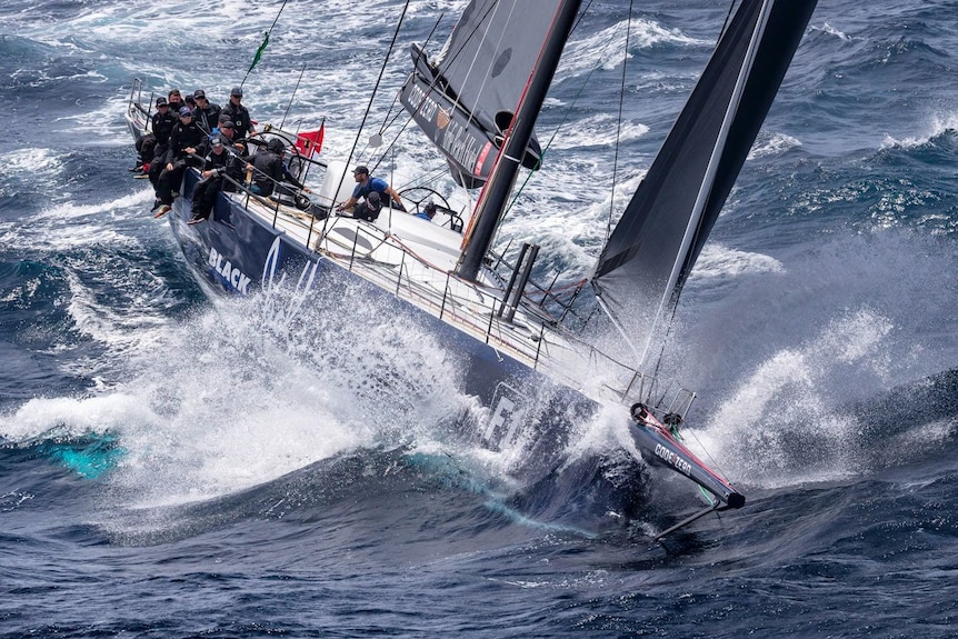 Crew on a black yacht hang their legs over the side