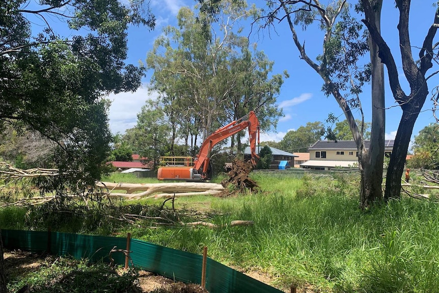 An excavator among housing clearing trees.