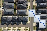 An aerial photo of a housing estate, overlaid with emoji showing a downward-shifting line chart.