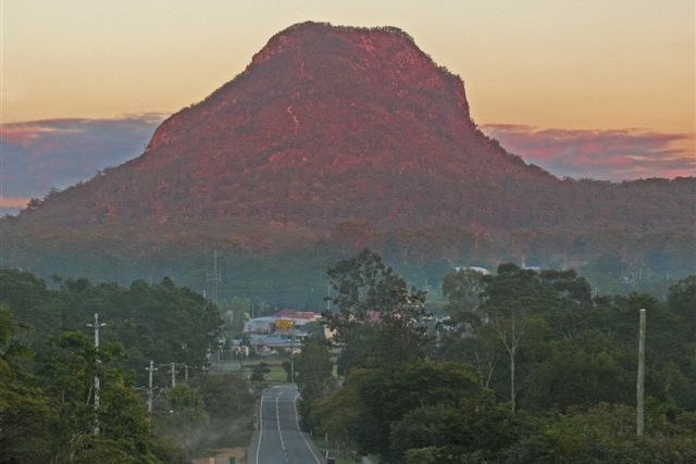 A mountain at sunset, with a road leading down to a town in the foreground.
