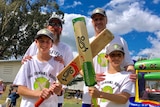 Two men stand behind their two young sons holding cricket bats.