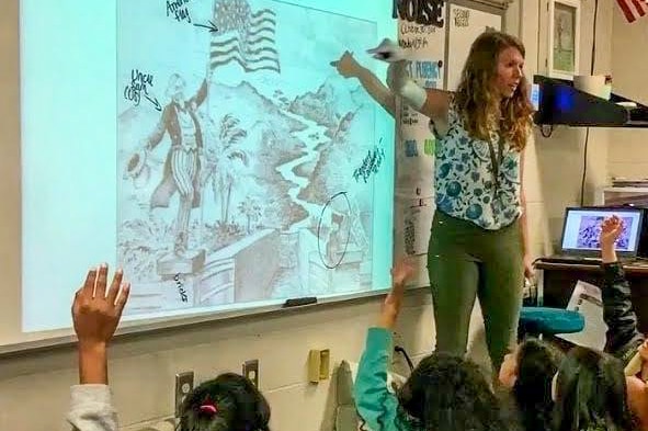 A young teacher at the front of the classroom surrounded by children