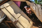 Woman crouches among rubble of a house