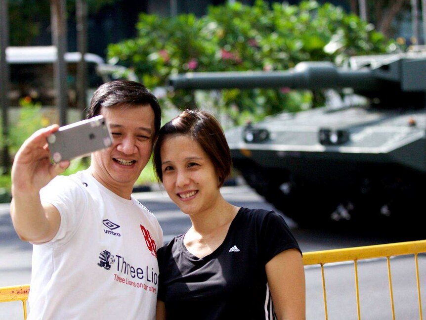 A couple pose for a selfie in front of a tank.
