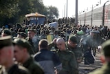 Men in uniform gather near a train station - it's a crowd shot 