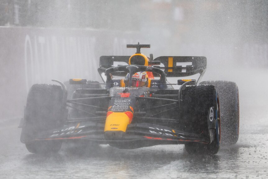 A driver in a dark blue F1 car, driving in the heavy rain.