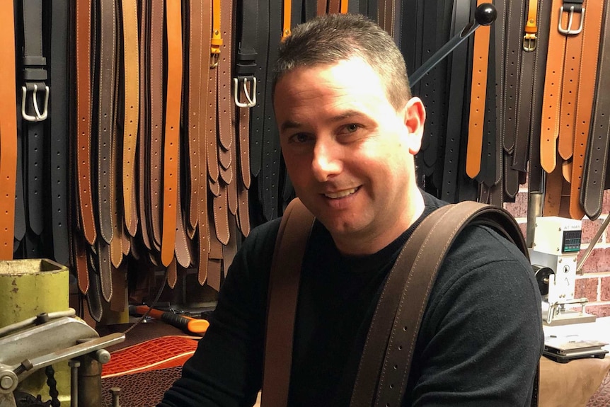 A man sits at a machine making leather belts