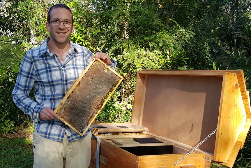 Chris Wyatt standing by an open hive with a frame of honey in his hands.