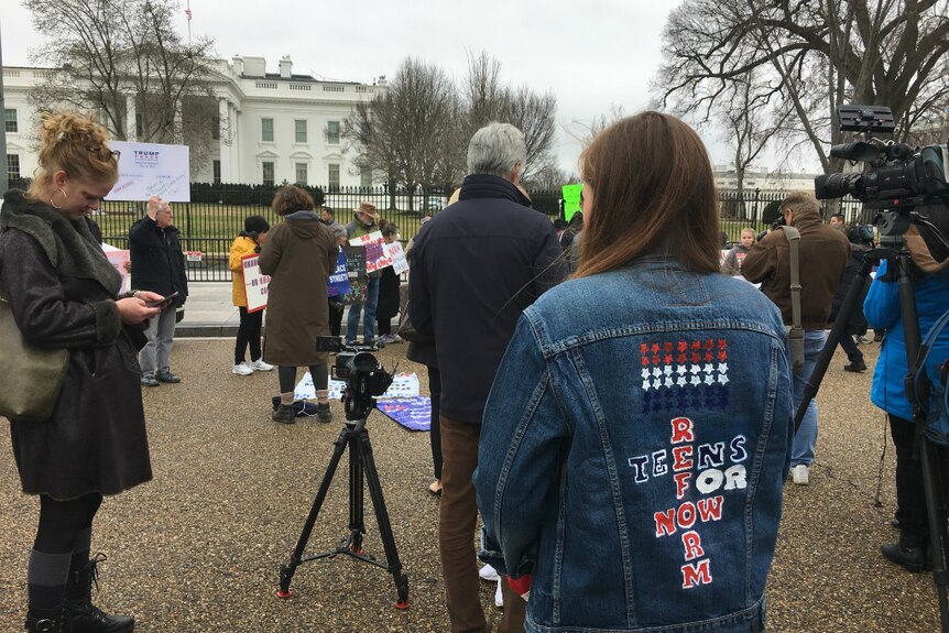 A young woman, whose face isn't visible, shows her hand-painted denim jacket that reads: teens for gun reform.