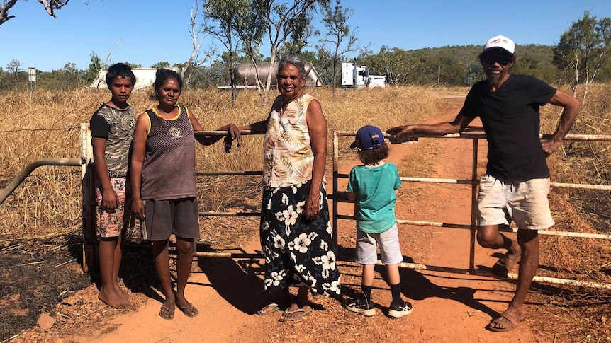 Woman stands with four other family members by fence of their property