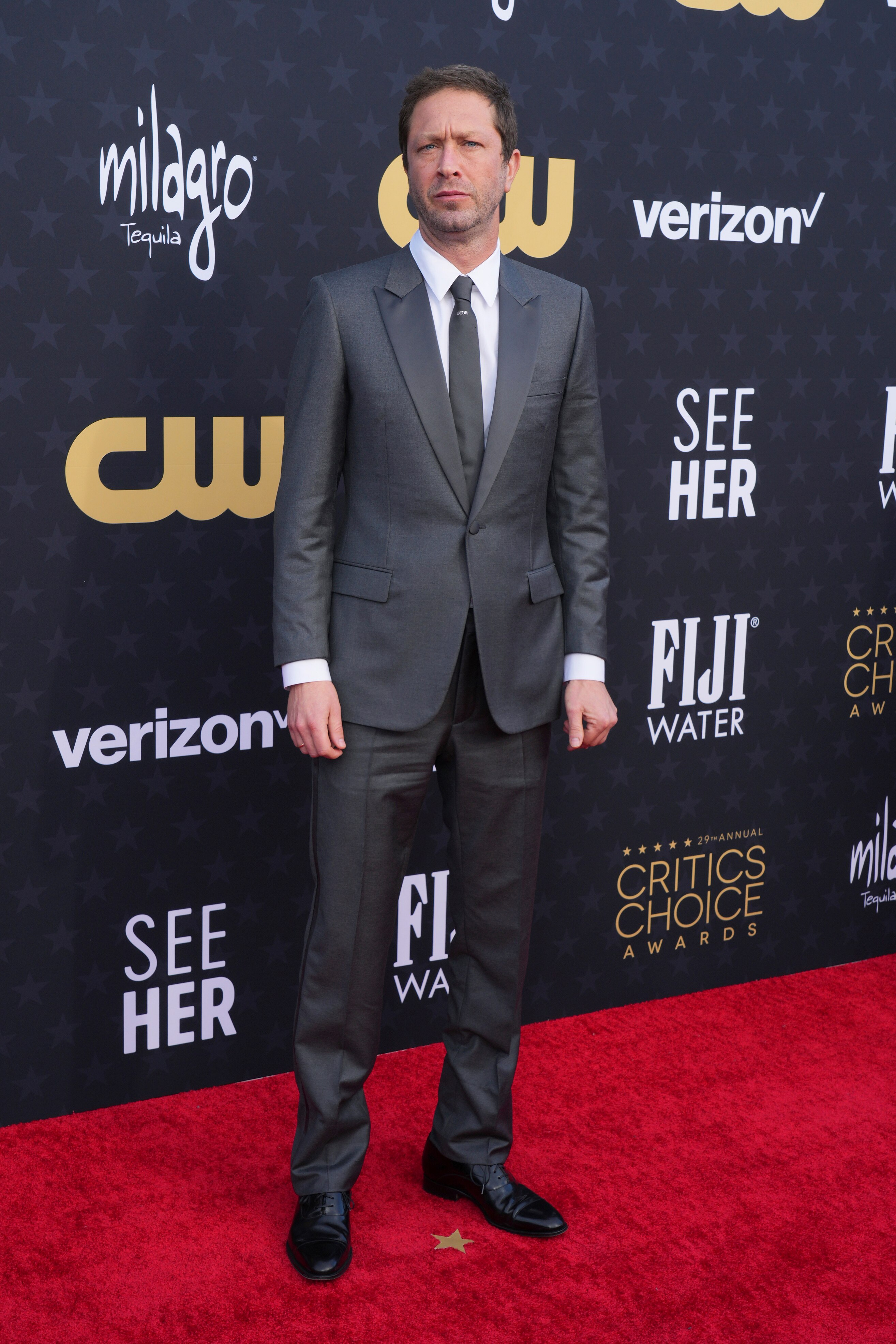 Ebon Moss-Bachrach wearing a grey suit with a white shirt and a grey tie