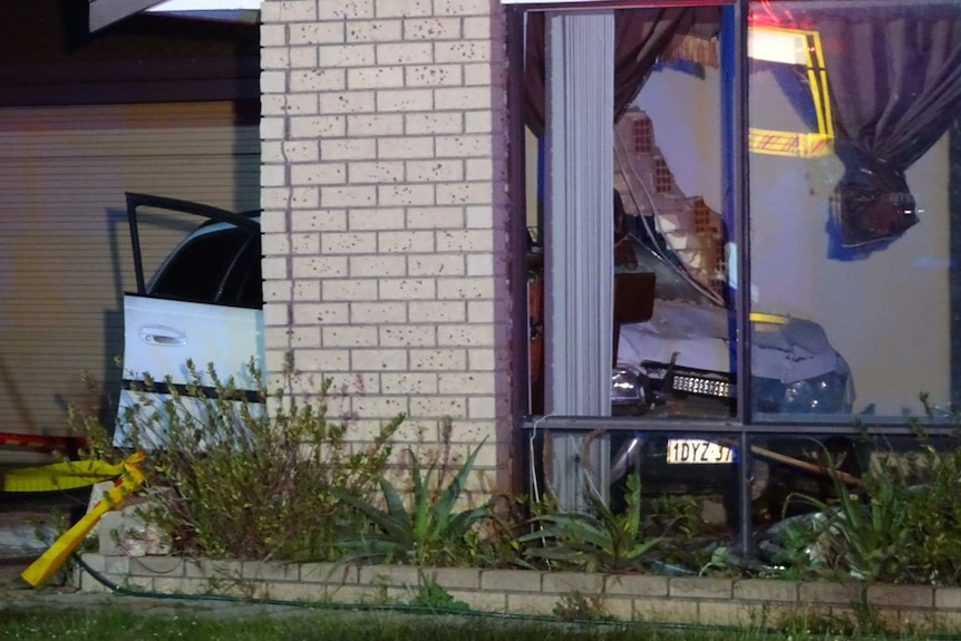 A picture of the room of a house with a crashed car jutting out of the wall and visible through the window.