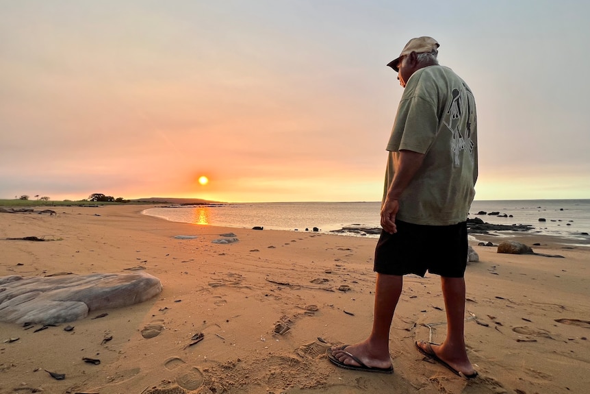 A man stands at a beach gazing at the sunset