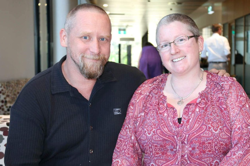 A man and a woman smile. The man has his arm around the woman.