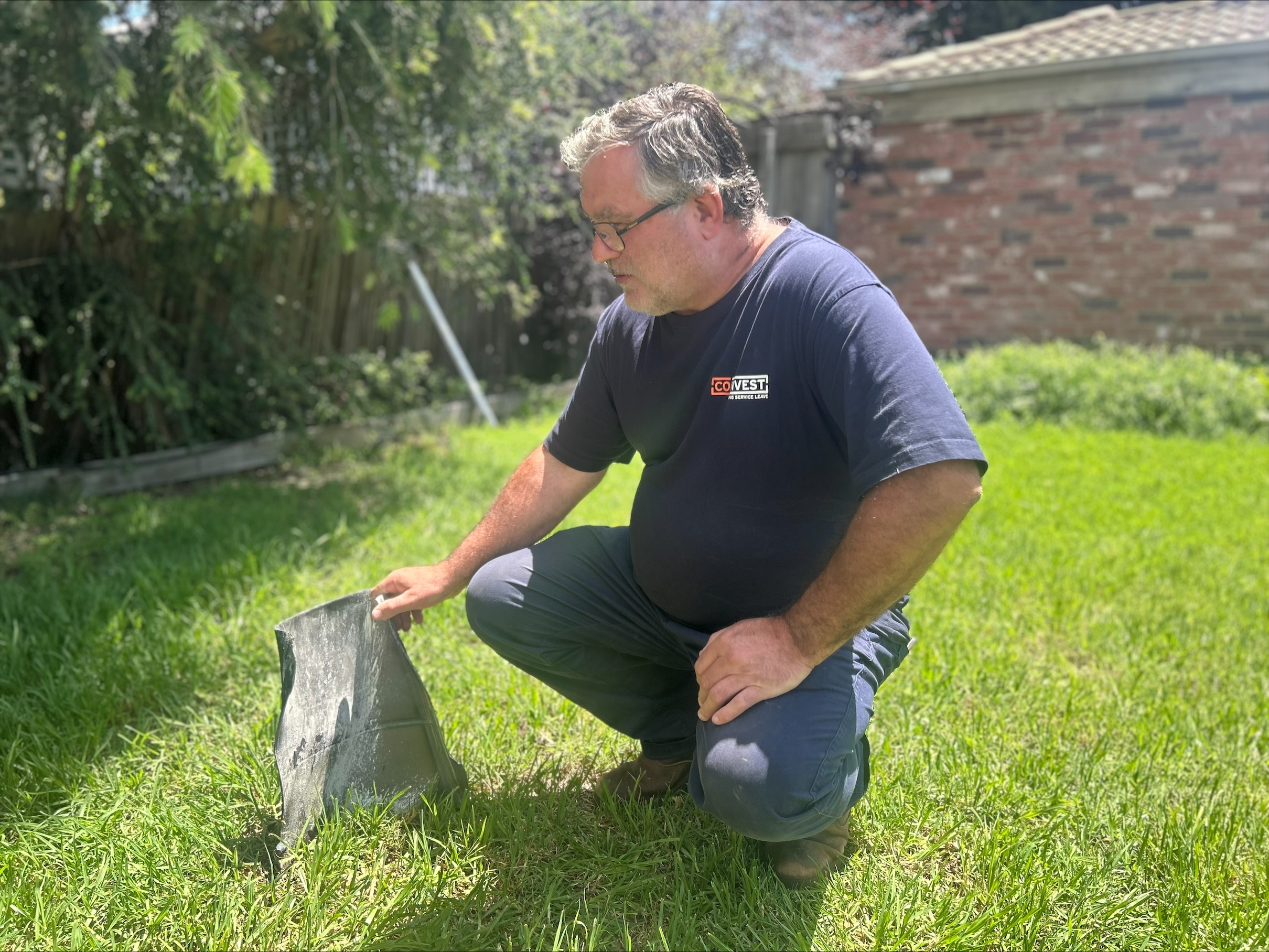 A man kneels on a lawn next to a large piece of metal.