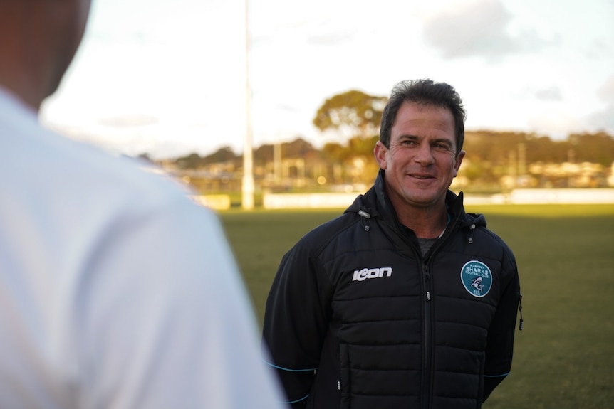 A man stands on a football field while being interviewed.