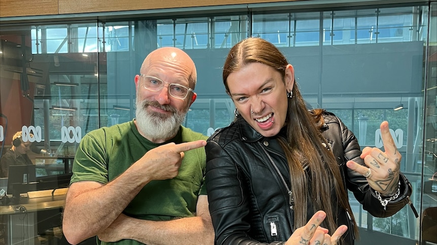 A man in a leather jacket makes the rock on symbol next to Raf Epstein, pointing at the other man